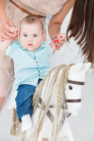 Una madre feliz ayuda a un pequeño hijo a montar un caballo de juguete . —  Fotos de Stock