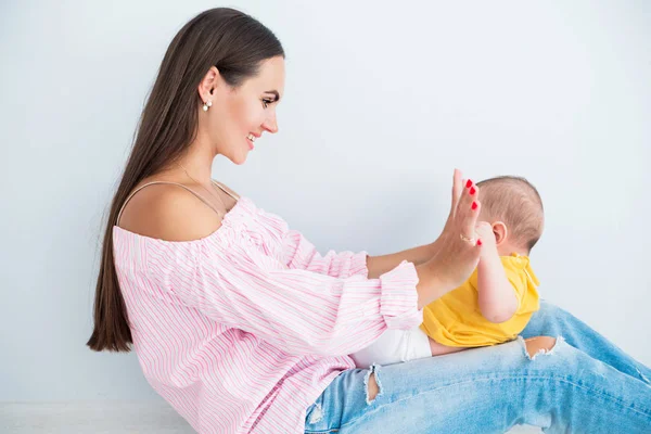 Feliz mãe senta-se no chão com seu pequeno filho em um fundo cinza — Fotografia de Stock