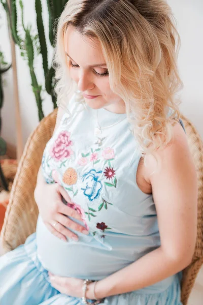 Mulher grávida em um vestido azul sentado em uma cadeira de vime — Fotografia de Stock