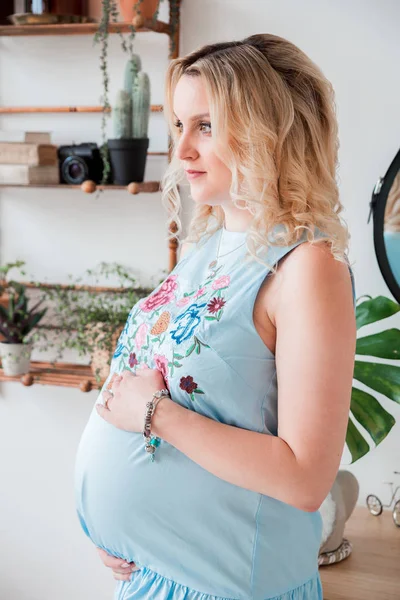 Blond dziewczyna w ciąży w niebieskiej sukni we wnętrzu pokoju — Zdjęcie stockowe