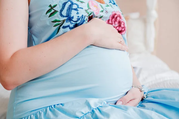 Una mujer embarazada en un vestido azul abraza su vientre —  Fotos de Stock