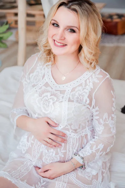Fille enceinte blonde en robe blanche assise sur le lit — Photo