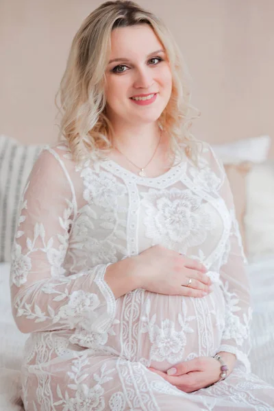 Grávida menina loira em vestido branco sentado na cama — Fotografia de Stock