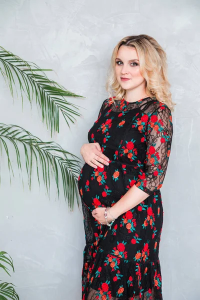 Kobieta w ciąży w czarnej sukni stoi na szarej ścianie i przytulanie jej brzuch — Zdjęcie stockowe