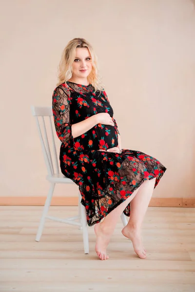 Mulher grávida sentada em uma cadeira em frente a uma parede de cor bege — Fotografia de Stock