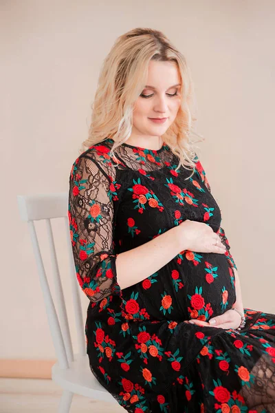Kobieta w ciąży siedzi na krześle naprzeciwko beżowy kolor ściany — Zdjęcie stockowe