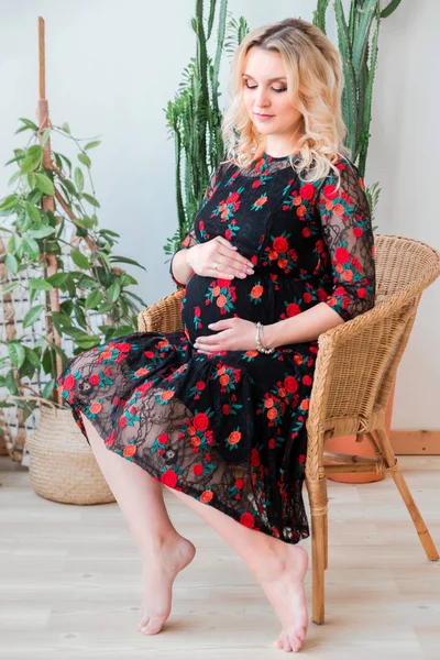 Mulher grávida em um vestido preto sentado em uma cadeira de vime — Fotografia de Stock