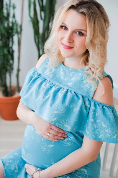 Gravid kvinna i en blå klänning kramar hennes mage — Stockfoto