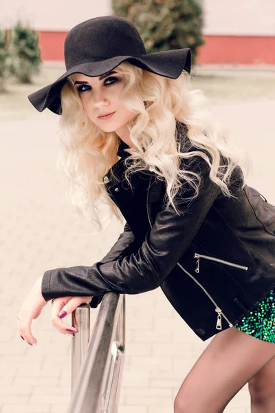 Girl in a black hat and a leather jacket is standing, leaning on the railing — Stock Photo, Image