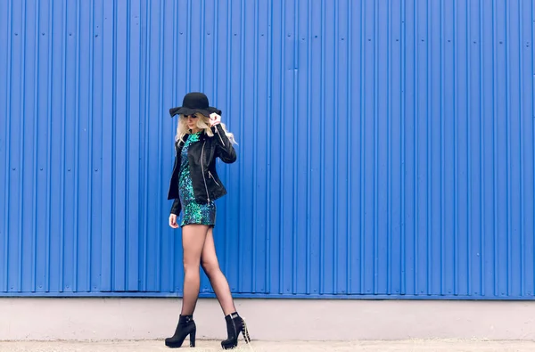 La fille au chapeau noir et à la veste en cuir longe le mur bleu — Photo