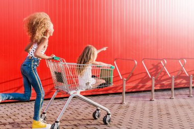 2 kız eğlenmek ve kırmızı bir duvarın arka planında bir bakkal arabası ile eğlenmek