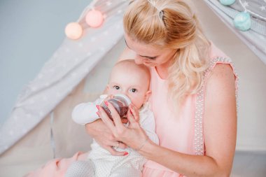 anne bir çocuk çadırı yakınındaki bir odada bir şişeden oğlunu besler