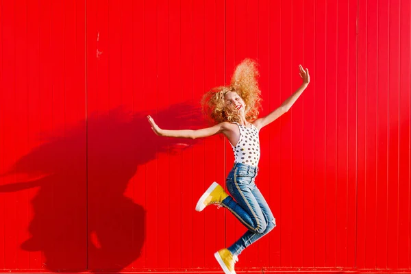Belle adolescente fait un saut sur le fond d'un mur rouge — Photo