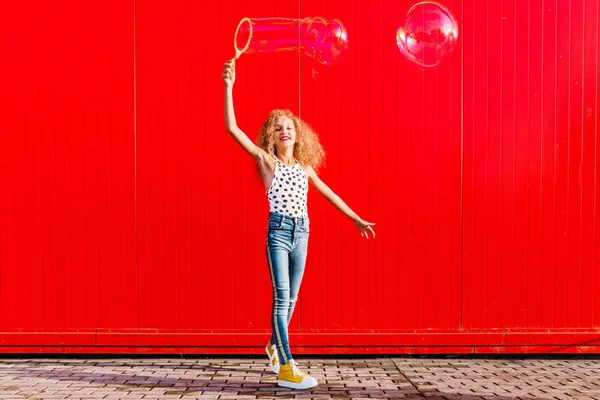 Belle adolescente gonfle bulles de savon contre le mur rouge — Photo