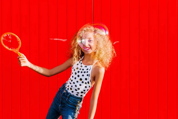 Hermosa adolescente infla burbujas de jabón contra la pared roja — Foto de Stock