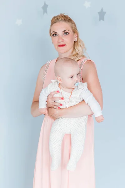 Mãe em um vestido rosa segura um pequeno filho em seus braços e olha para a câmera — Fotografia de Stock