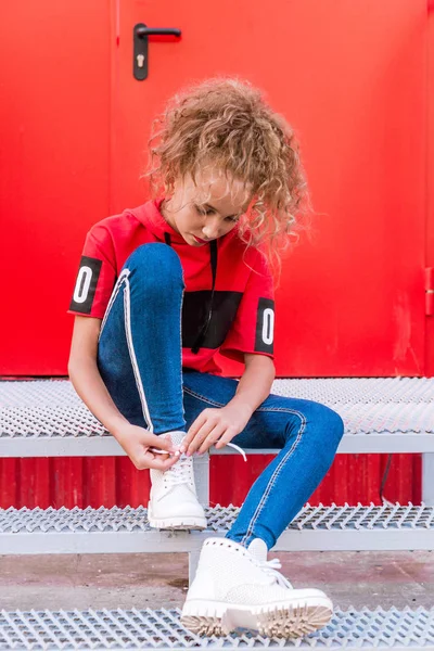 Adolescent à la mode fille posant sur un fond de mur rouge, assis sur les escaliers — Photo