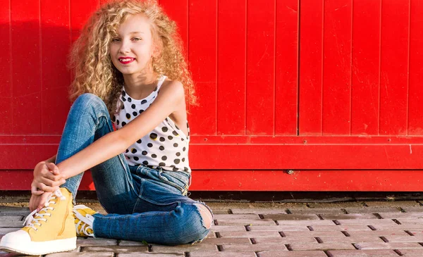Adolescent fille est assis contre un mur rouge sur une rue de la ville — Photo