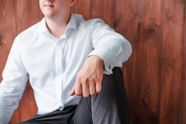 man in pants and shirt is sitting on the floor and posing against the background of a wooden wall
