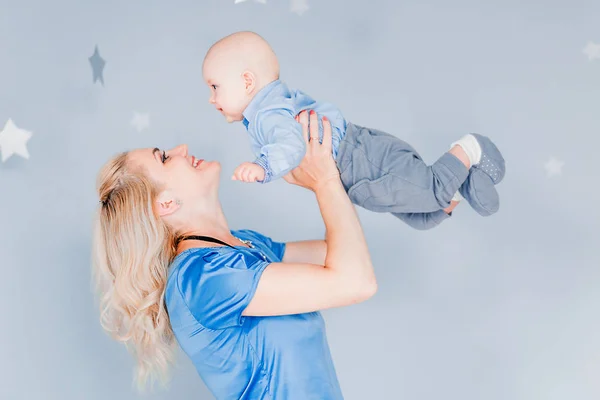 Mère joue et vomit un enfant dans la chambre des enfants sur le fond du mur bleu — Photo