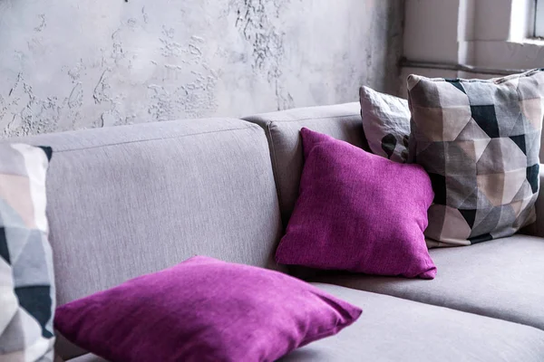 Canapé gris avec oreillers violets dans une chambre avec un mur gris — Photo