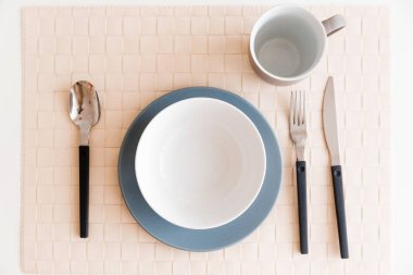 Masanın üzerinde bir tabak, kupa, çatal bıçak takımı var. Üstte görüntü