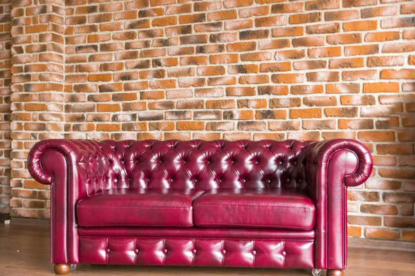 Sofá de couro vermelho fica no fundo da parede de tijolo . — Fotografia de Stock