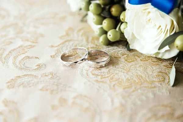 Anéis de casamento jazem no tecido ao lado de um monte de flores — Fotografia de Stock