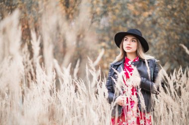 Kırmızı elbise ve siyah ceket güzel kız alanında uzun boylu çim arasında yürüyor