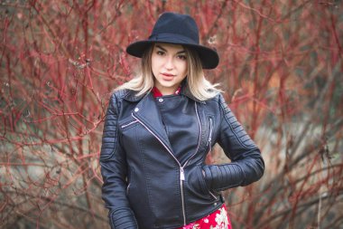 Kırmızı elbise ve siyah ceket güzel kız bir sonbahar çalı arka plan karşı poz