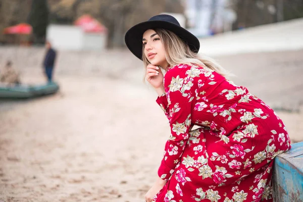 Beautiful girl in a red dress and black jacket sits on a blue boat — Stock Photo, Image