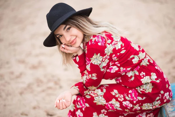 Beautiful girl in a red dress and black jacket sits on a blue boat — Stock Photo, Image