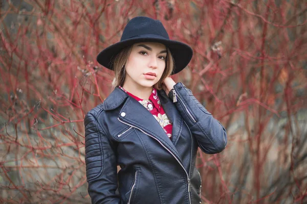 Schönes Mädchen in rotem Kleid und schwarzer Jacke posiert vor dem Hintergrund eines Herbstbusches — Stockfoto