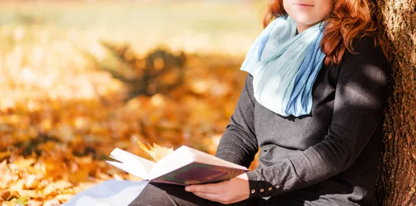 Junge Frau sitzt unter einem Baum und liest im Herbstpark ein Buch — Stockfoto