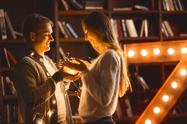 Влюбленная пара в уютной комнате с большой лампой в виде письма и рождественских огней — стоковое фото
