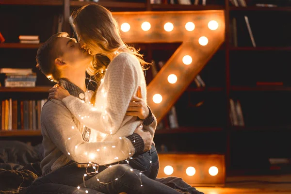 Couple in love in a cozy room with a large lamp in the form of a letter and Christmas lights — Stock Photo, Image