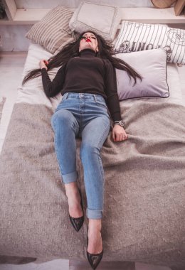 Siyah kazaklı ve kot pantolonlu güzel bir kız yatakta poz veriyor.