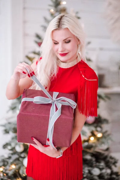 Όμορφη ξανθιά κοπέλα με ένα δώρο Πρωτοχρονιάς στα χέρια κοντά στο χριστουγεννιάτικο δέντρο — Φωτογραφία Αρχείου