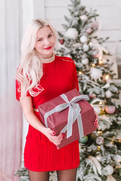 Hermosa chica rubia con un regalo de Año Nuevo en las manos cerca del árbol de Navidad — Foto de Stock