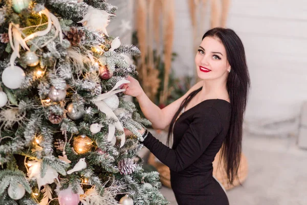 Девушка в черном платье позирует возле новогодней елки — стоковое фото