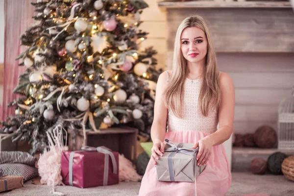 Девушка в розовом платье позирует с подарком возле новогодней елки — стоковое фото