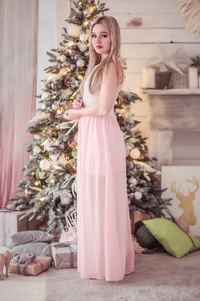 Krásná dívka v růžových šatech pózuje v blízkosti novoroční strom — Stock fotografie