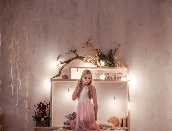 Retrato de jovem bela mulher loira relaxar no quarto. Sorria menina caucasiana feliz com cabelo encaracolado longo usar vestido rosa — Fotografia de Stock