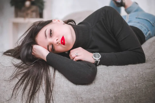 Beautiful girl in a black sweater and blue jeans posing on the bed — Stock Photo, Image