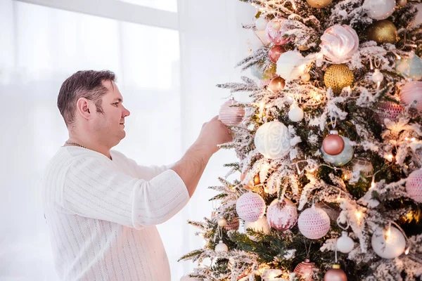 Um homem com uma camisola branca decora uma árvore de Natal — Fotografia de Stock