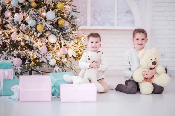 Um menino e uma menina sentam-se ao lado de presentes de Ano Novo e uma árvore de Natal e olham para a câmera — Fotografia de Stock