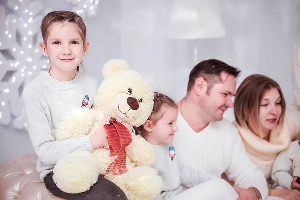 Rodzina w noworocznym wnętrzu. Dziewczyna w zabawkowym misiu patrzy w kamerę — Zdjęcie stockowe
