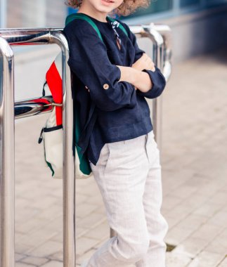 Açık pantolonlu ve elinde sırt çantasıyla poz veren koyu renk gömlekli bir öğrenci. Vertycal fotoğraf