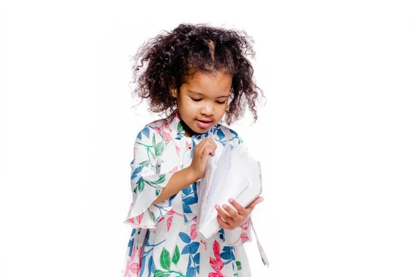 Pequeña chica afroamericana bastante de moda en vestido floral blanco mirando el cuaderno — Foto de Stock