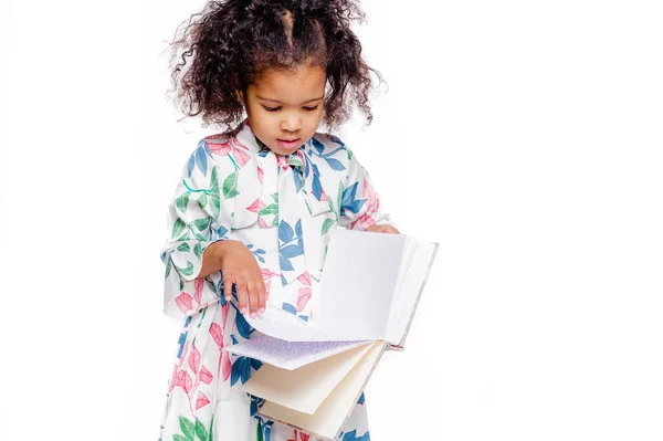 Pequeña chica afroamericana bastante de moda en vestido floral blanco mirando el cuaderno — Foto de Stock
